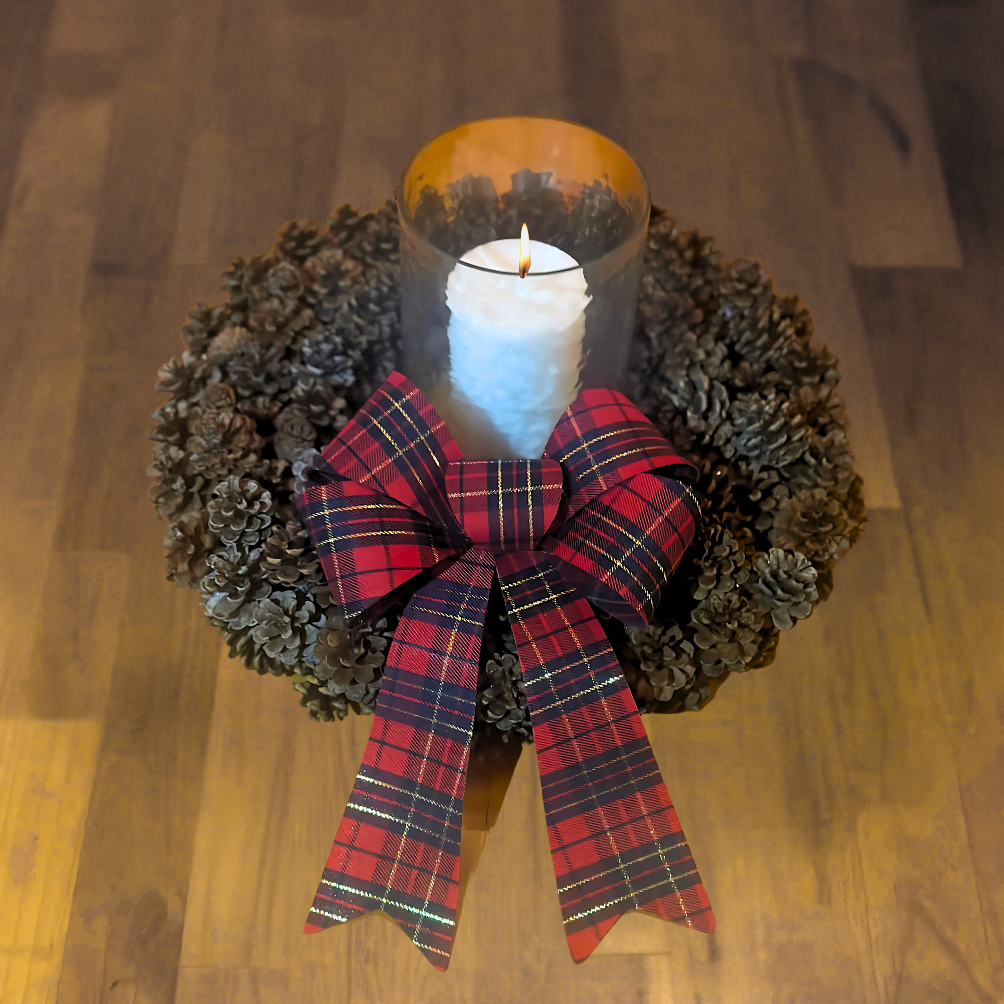 Decorative AuSable wreath with a candle and plaid bow on a wooden surface